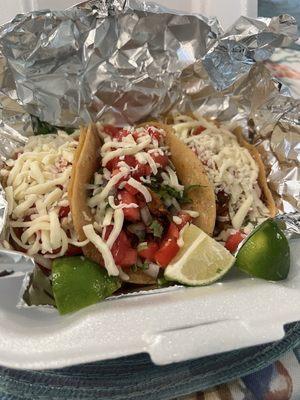 Chicken tacos with cheese, cilantro and onions, tomatoes, and limes