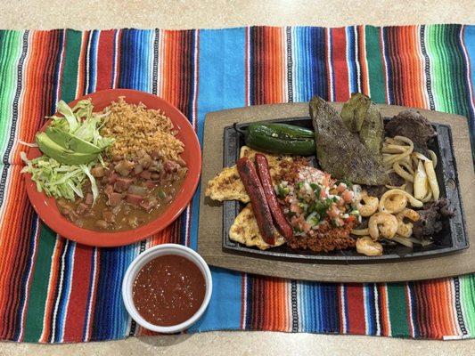 El Comal- Carne Asada, chicken, grilled nopales, sausage, jalapeño, shrimp & onions. Topped w/ choriqueso & pico. Rice, beans, lettuce.