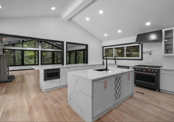 Elegant kitchen with twin black sinks, twin dishwashers, in cabinet microwave, pot filler over range, all black appliances trimmed in copper