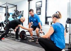 Both Trainer and physical therapist are collaborating to assist a client with  a complex strength exercise.