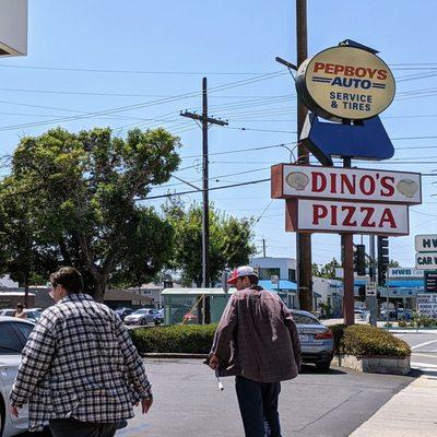 Corner sign of Dino's Pizza, shared with Pep Boys, along with their parking lot