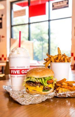 A Five Guys cheeseburger, milkshake and regular order of fries sits on a table inside a Five Guys restaurant.