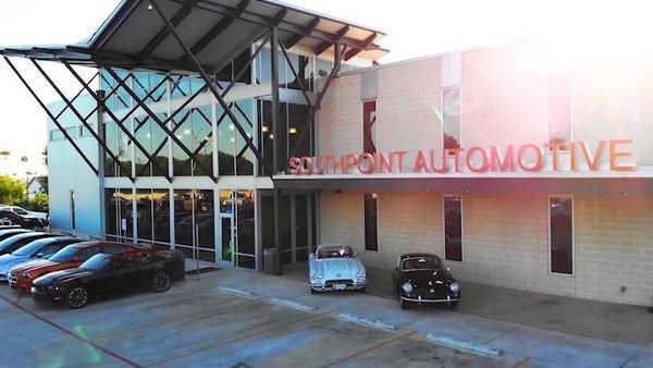 A golden sunset casts a warm glow on the modern facade of Southpoint Automotive, showcasing a lineup of classic cars.