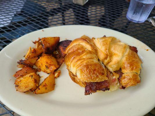 Croissant egg sandwich with bacon and home potatoes.