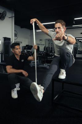 Coach Josh and Nate working together on elevated pistol squats to boost single-leg squat mobility.