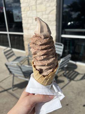 Chocolate soft serve with chocolate almonds in a waffle cone