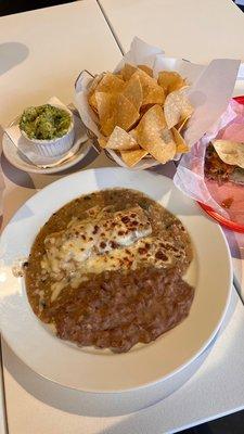 Beef brisket enchilada with pork green chili sauce and a side of veggie refried beans, carnita taco, and chips & guac