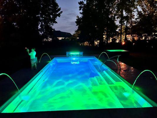 Outdoor pool with waterfall features, spa, lighting, and benches.