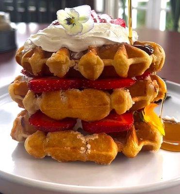 Golden-brown waffles, layered with fresh strawberries, a dollop of whipped cream, and a drizzle of maple syrup.