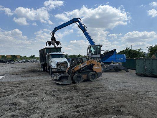 A Gardner Metal Recycling Mack roll off dumpster truck and Case skid steer and Fuchs material handler