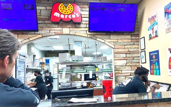 Inside.  Notice young man behind counter on phone placing orders.  Two people to the left in kitchen making pizzas.