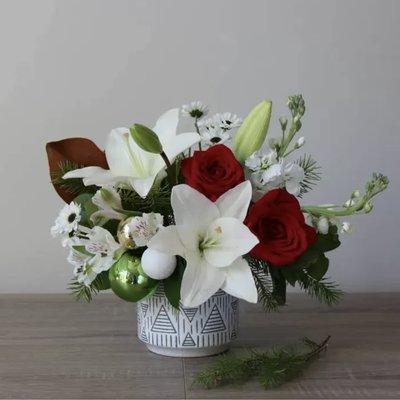 A beautiful festive bouquet of roses, stock and lilies, accented with ornaments and designed in a large keepsake ceramic pot.