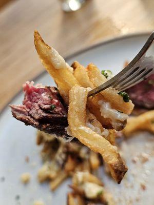 A fork holding a piece of the Hanger Steak and fries.