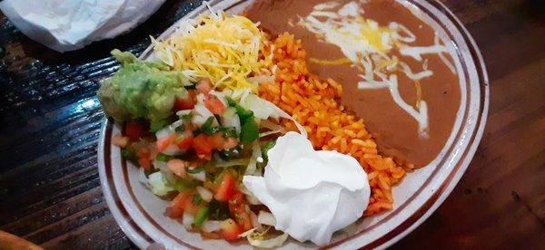 A side of rice, refried beans, picante sauce, shredded cheese and sour cream.