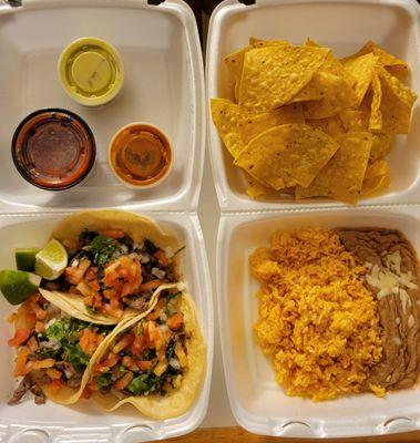 Three Asada tacos with beans, rice, chips, and salsa.