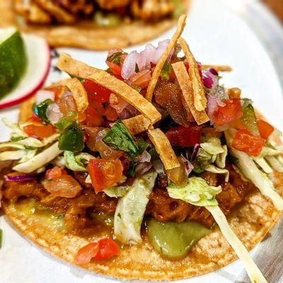 Young Jackfruit: Braised Jackfruit in a Citrus Soy Marinade with Vegan Avocado Crema, Pico de Gallo, Salsa Verde Slaw, and Tortilla Strips.