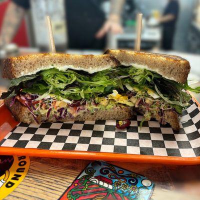 House sourdough spread with vegan poppy seed mayo, and loaded high with spring mix, avocado, Froma tomato, sprouts, and house crushed legume