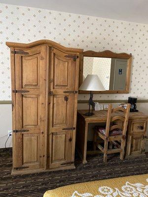 Bureau with TV, desk and chair with lamp, coffee maker and a mirror on the wall.