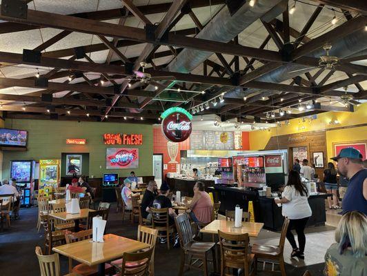 Classic open concept restaurant with wood table tops , centrally located fixins bar and drinks , to the right is the famous bakery