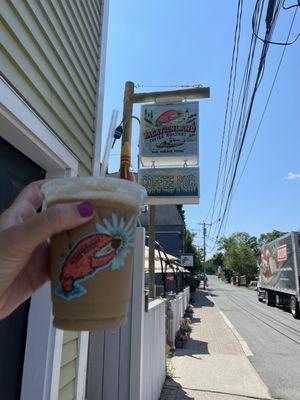 Iced latte in front of the sign for the location