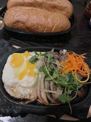 Eat breakfast the Vietnamese way! Seared steak with sunny side eggs, Banh mi, and pate. All served on a sizzling hot plate!