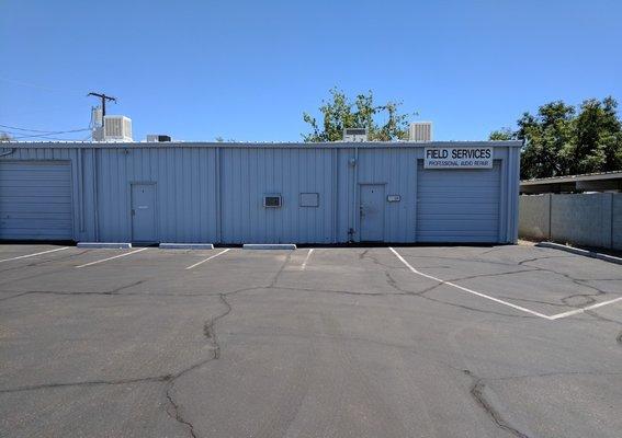 Field Services shop - entrance is the small door to the left of the overhead sign. July 2018.