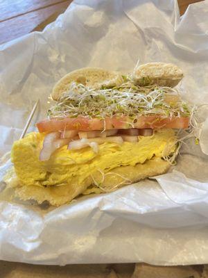 Breakfast sandwich on a plain bagel with Gouda, sprouts, red onion, and tomato.