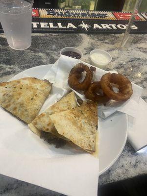 Quesadilla and burnt onion rings still oozing grease after setting on a napkin because of the puddle on the plate