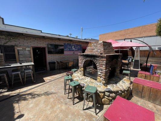 Outdoor seating with wood fireplace and two big screen TVs.