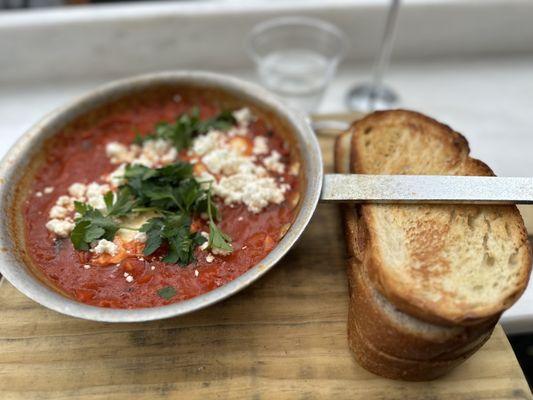 Shakshuka served in the pan with three slices of challah.