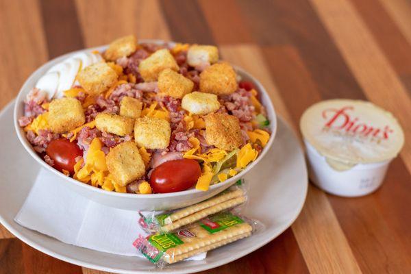 A half chef salad with a side of ranch dressing and crackers.