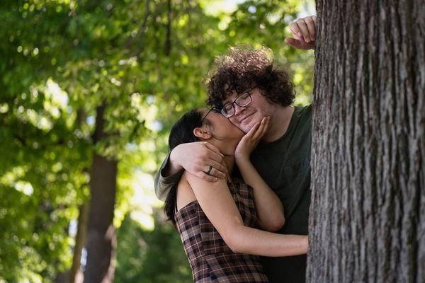 Intimate moment between interracial couple in a park behind a tree