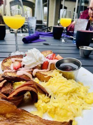 Strawberry shortcake French toast , eggs, and bacon. Mimosas in background.