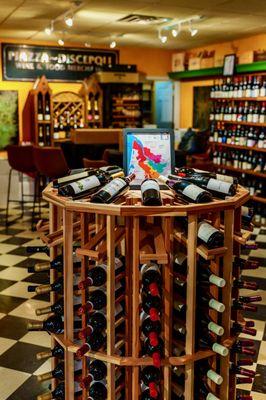 Large selection of red wines on a circular wine rack and on shelves lining a wall.  Champagne shelf in the background.