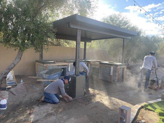 Solid roof patio cover with BBQ and travertine patio under construction.