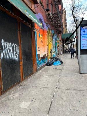 Entrance to Icon Apartments on troubled corner with abandoned businesses, trash and homeless.