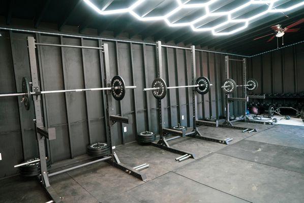 Weight room with squat racks with olympic style weights, hex bars, and dumbbells for strength and power.