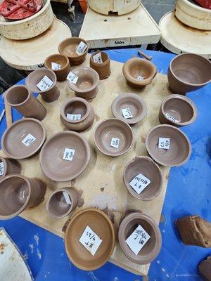 Close up photo of all the clay pieces made by the class, mostly shaped as small bowls, cups, and pots