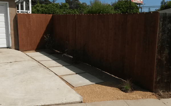 Poured concrete squares with decomposed granite between pavers and stained fence with gate