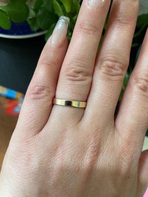 A left hand with a simple flat gold band on the ring finger.