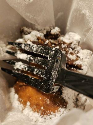 The Fried Oreos inside a box with white paper and a black plastic fork to eat them with.