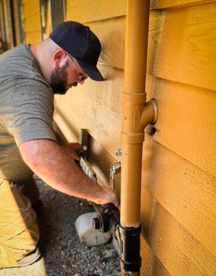 one of our licensed plumbers installing a pipe, expertly matching the color to blend seamlessly with the house's exterior.