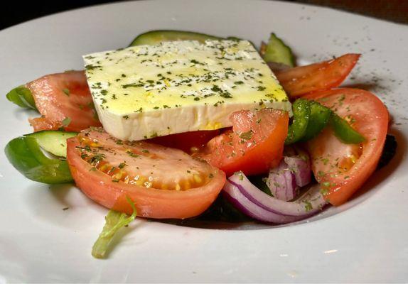 Greek salad with a bit of lettuce, lots of tomatoes, onions, cucumber and a slice of seasoned feta cheese.