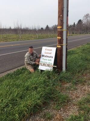 Warfield Farms sign with owner kneeling next to it.