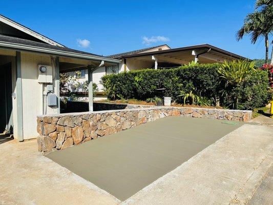 Rock wall with concrete parking pad around encased water valve and sloped flush with sidewalk and driveway