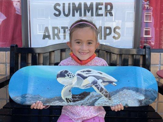 6 year old student showing her  painting of a sea turtle she made with acrylics on a skateboard, 2021