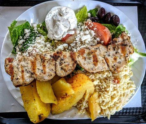 Chicken Souvlaki Dinner is served with Greek salad, rice pilaf, Greek potatoes, pita, and tzatziki sauce.