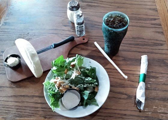 This is the beginning of the meal - Caesar salad, bread, and a soft drink.