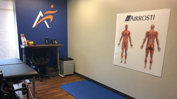 A look into the recovery room at Airrosti Keller. Exercise mats are on the floor and musculoskeletal diagrams are displayed on the walls.