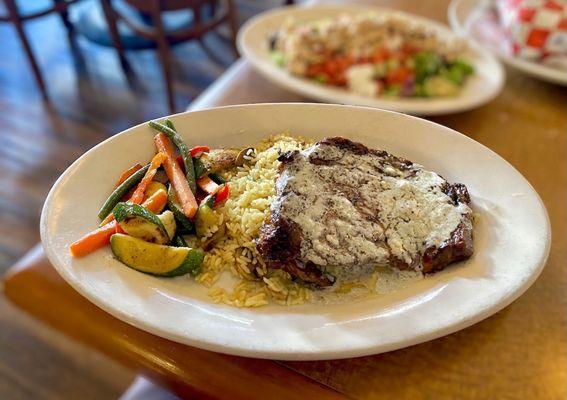 Ribeye steak topped with blue cheese over rice pilaf and vegetables.